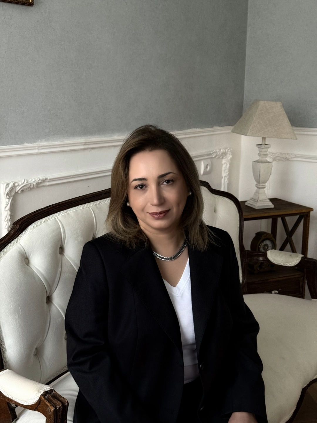 Аида Гасымова сидит на светлом диване в кабинете с голубыми стенами